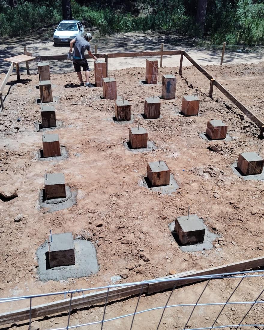 Foundation of concrete piers on the sandy plot, surrounded by pines.