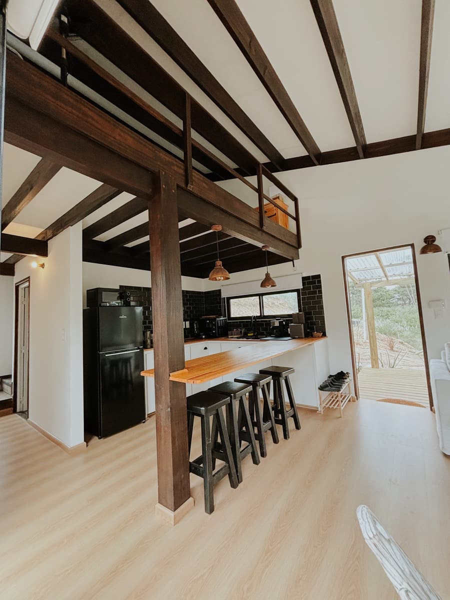 Open living space with dark ceiling beams, a kitchen and a wooden counter.