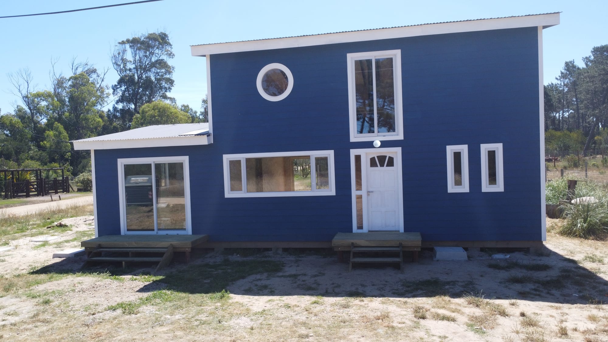 Front facade of Casa Azul: a two-storey timber house in blue with white window frames, a round porthole window and two timber terraces.