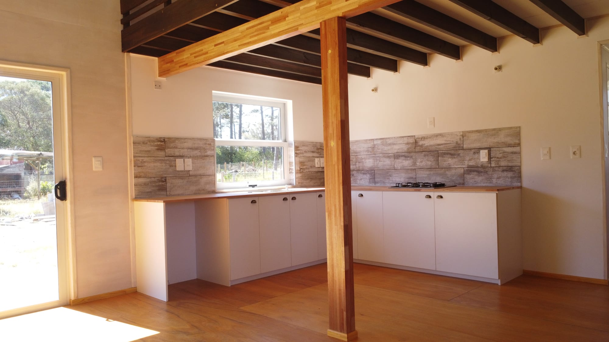 Corner kitchen of Casa Azul with a timber post in the middle, dark exposed beams and white base cabinets.