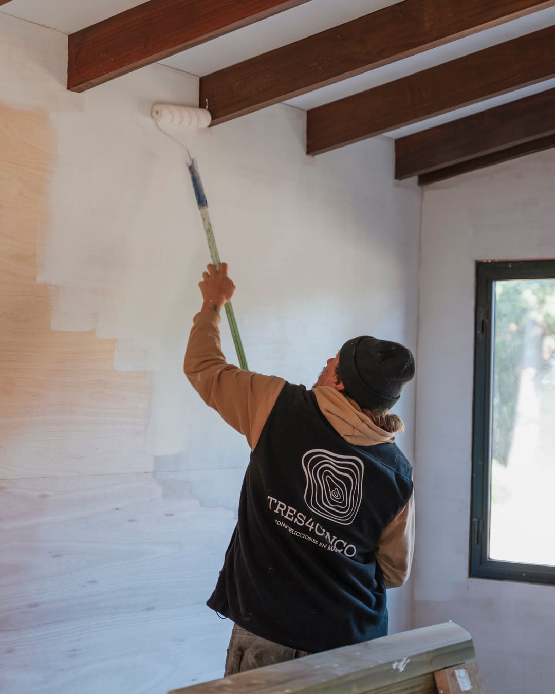 Worker in a TRES4CINCO vest rolling white paint onto the wall.