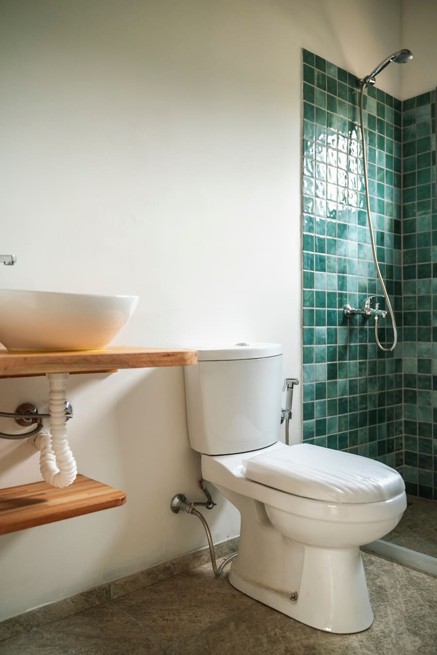 Bathroom with a countertop basin on a timber shelf, toilet and green-tiled shower.