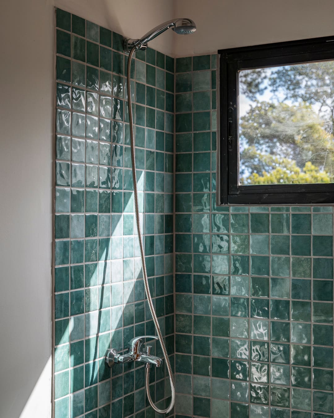 Shower with green glazed tiles, hand shower and a black window.