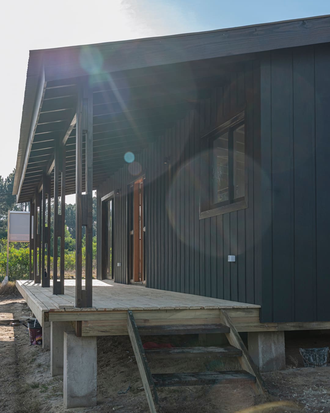 View along the veranda against the light, timber steps and the black facade in front.