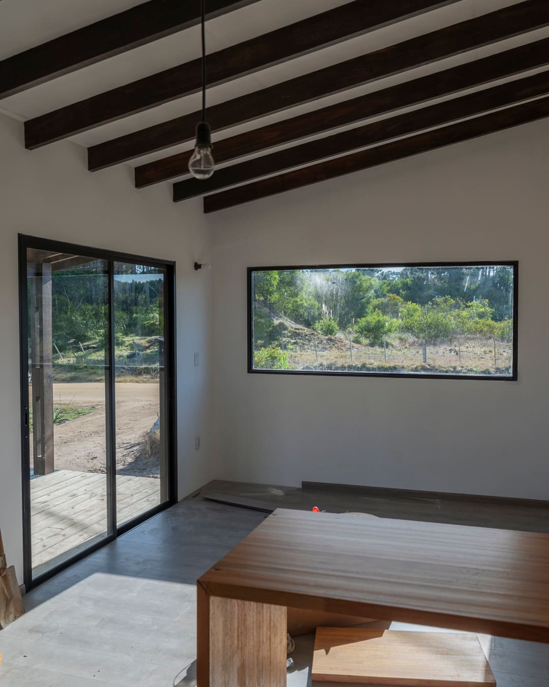 Living room with a sliding door to the veranda and a wide picture window, dark roof beams above.