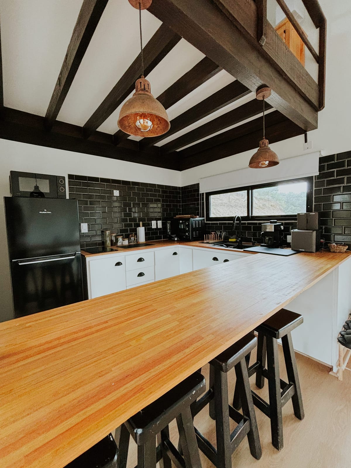Kitchen at Matipipe with a warm timber counter, black tiles and copper light fixtures.