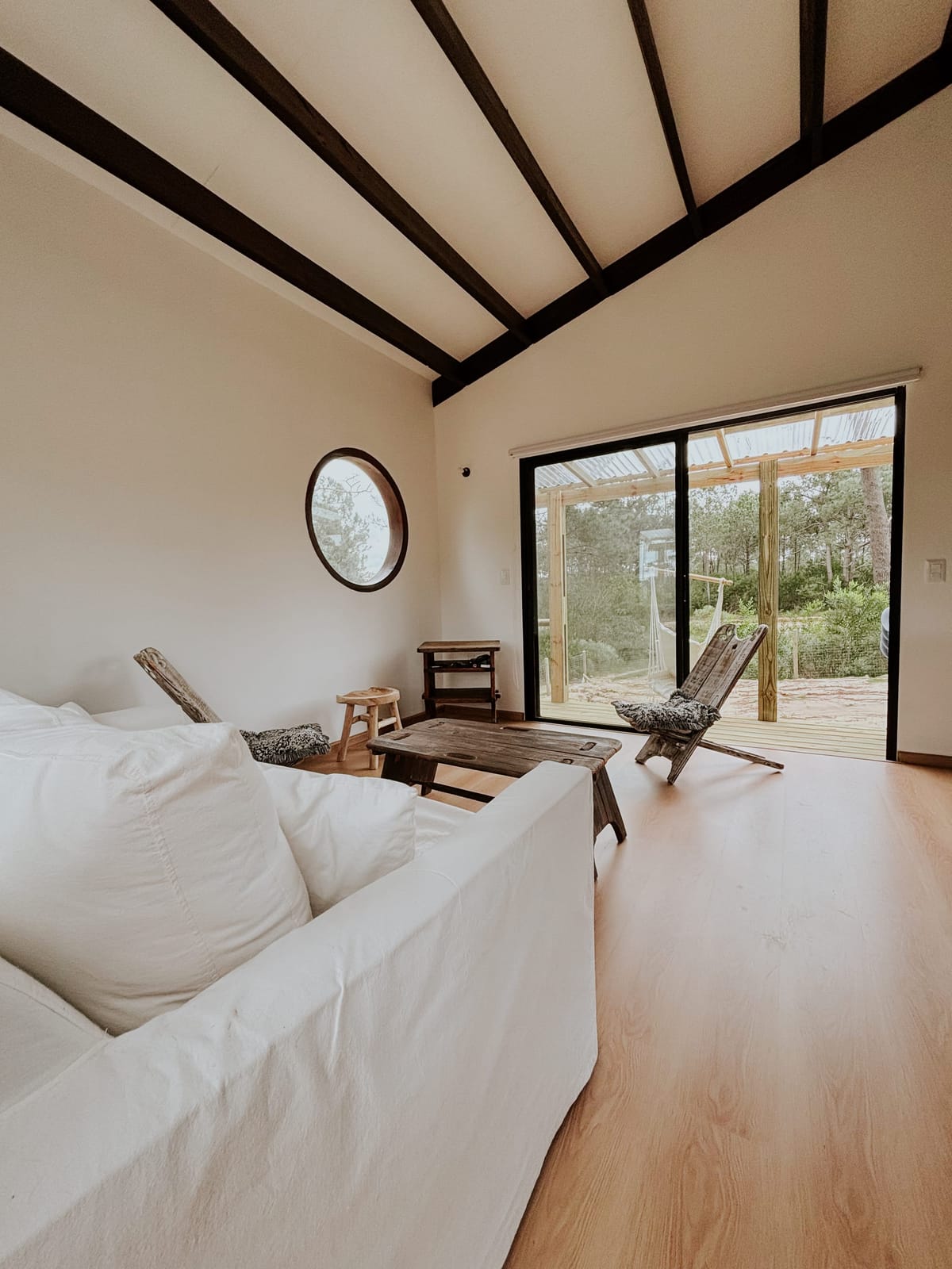 Living room at Matipipe with a white sofa, round porthole window and sliding door to the terrace.