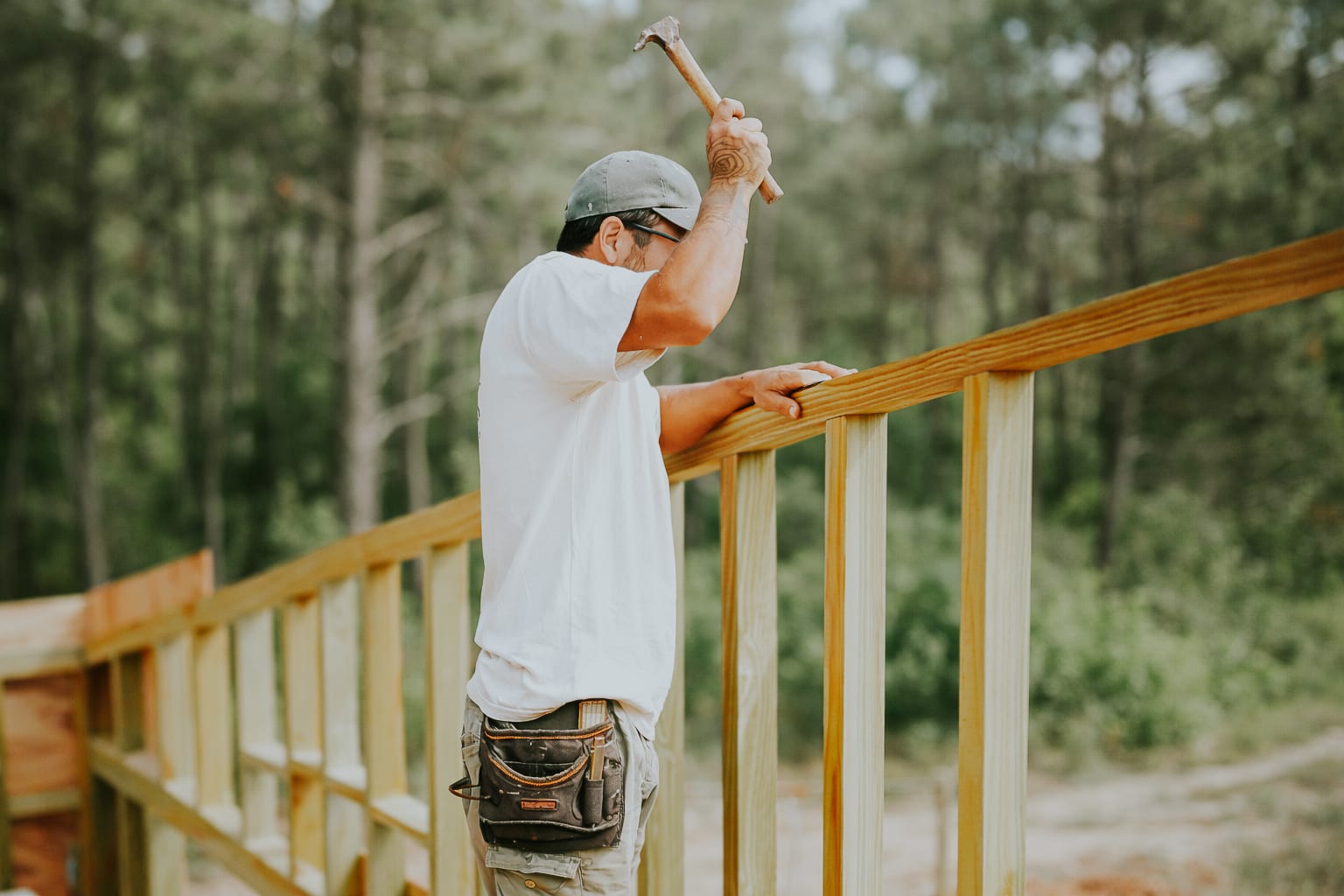 A carpenter raises his hammer over a timber frame, pine forest in the background.