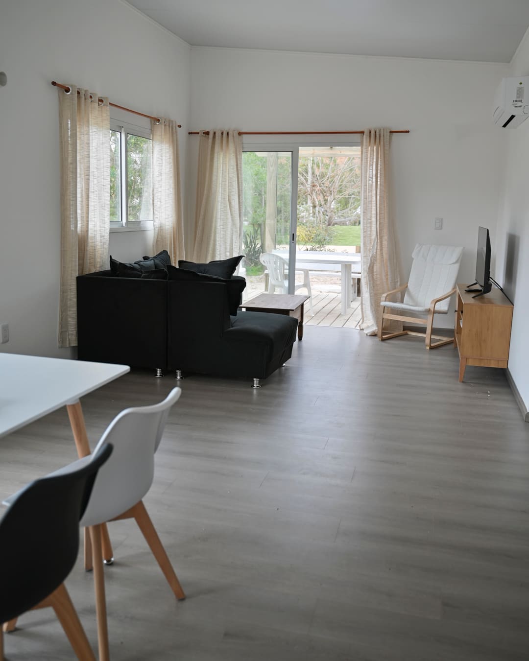 Bright living room with a black sofa, curtains and a sliding glass door opening onto the wooden deck.