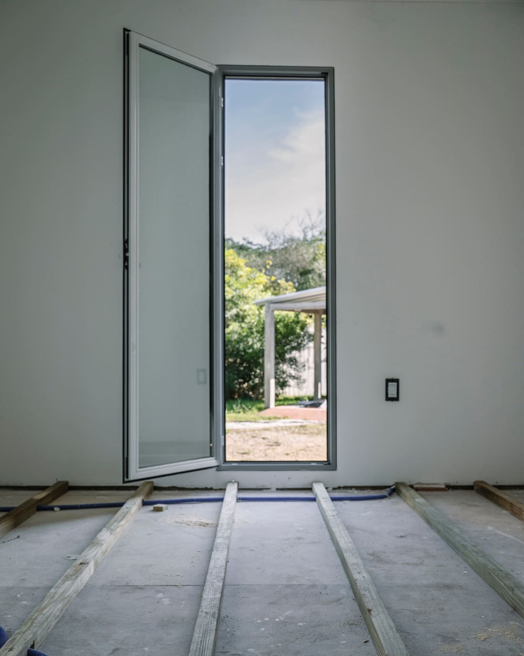 Tall open glass door looking out to the garden, with wooden battens on the bare floor in front.