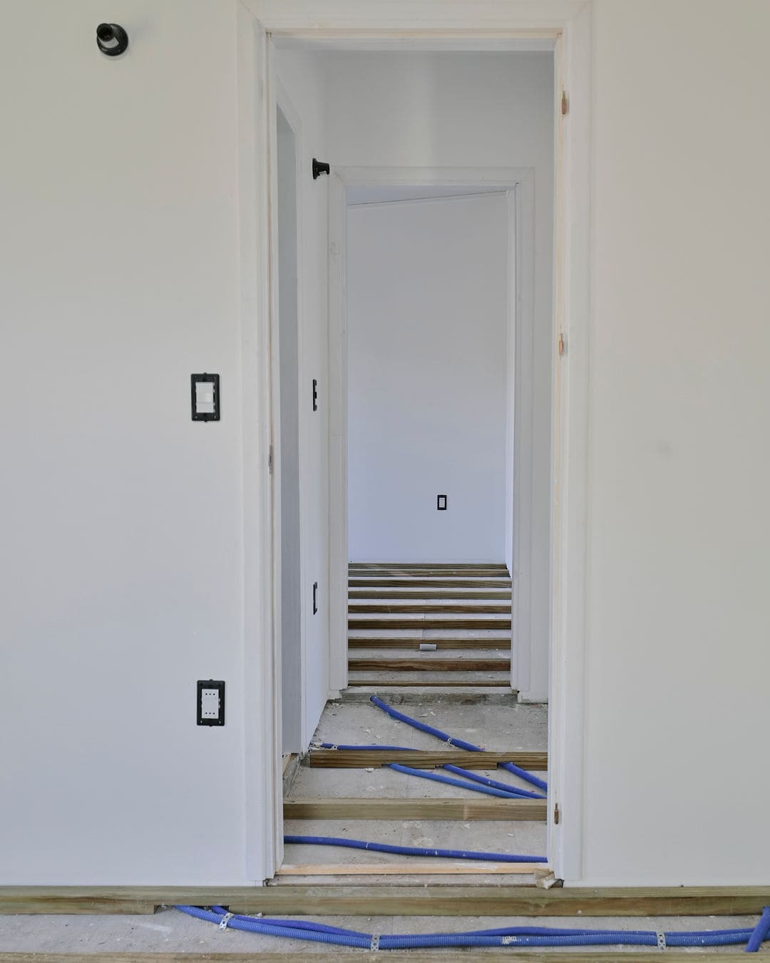 View through white door frames down a hallway, with wooden battens and blue pipes on the floor.
