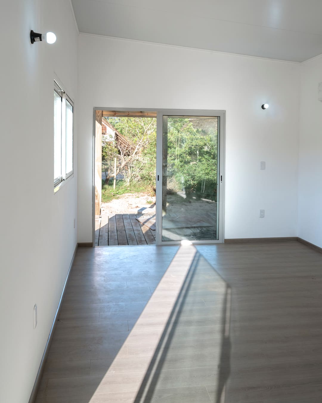 Empty bright room with a laminate floor and a sliding glass door leading to the wooden deck.