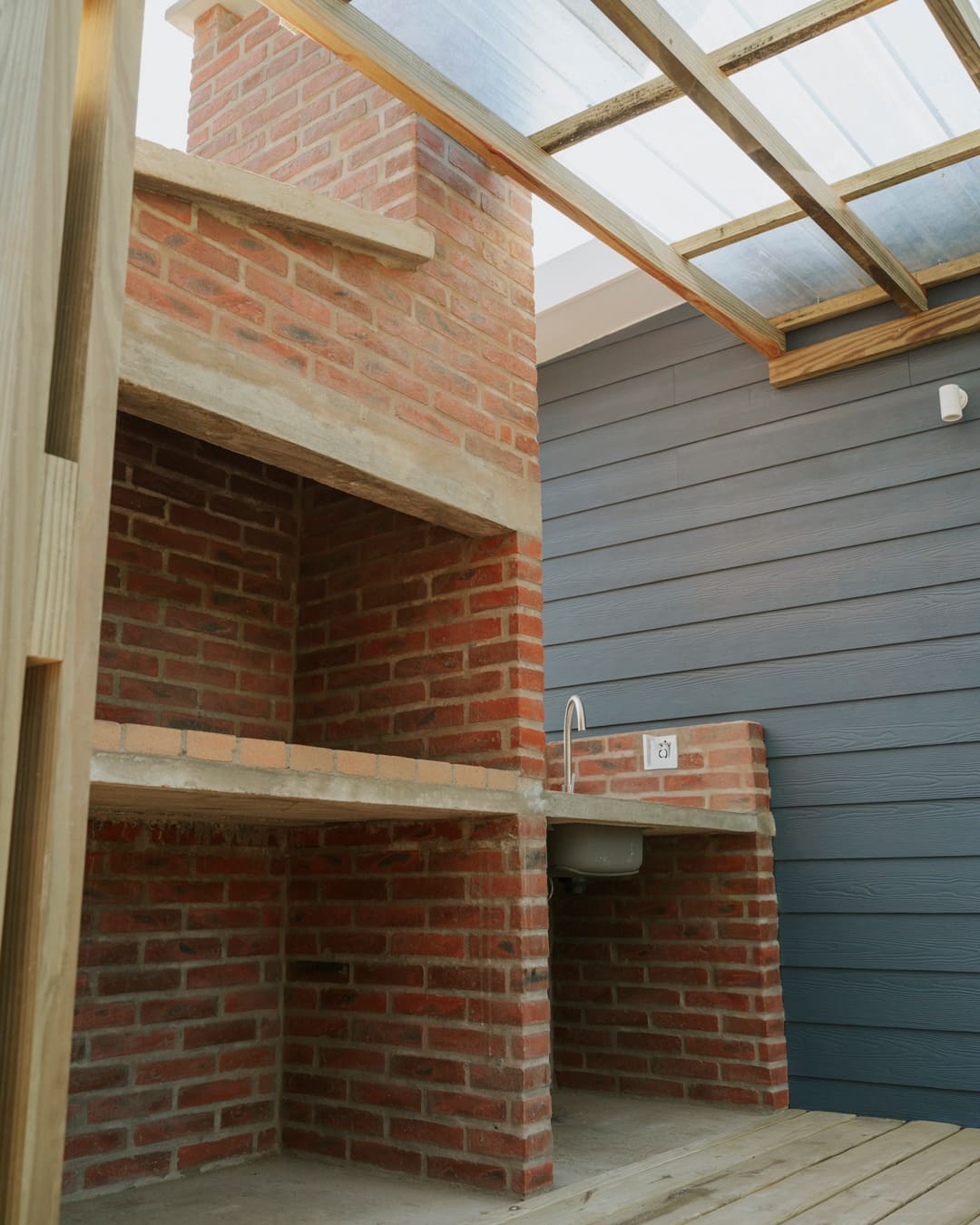 Brick barbecue with a chimney and a small sink with a tap beneath the pergola.